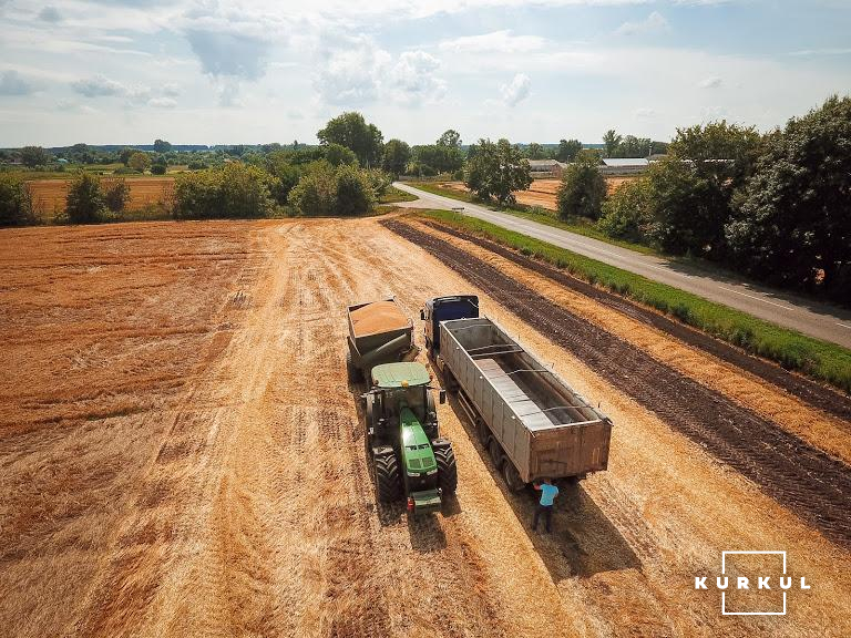 Трактор John Deere в агретуванні з бункером-перевантажувачем доставляє зерно до вантажівки